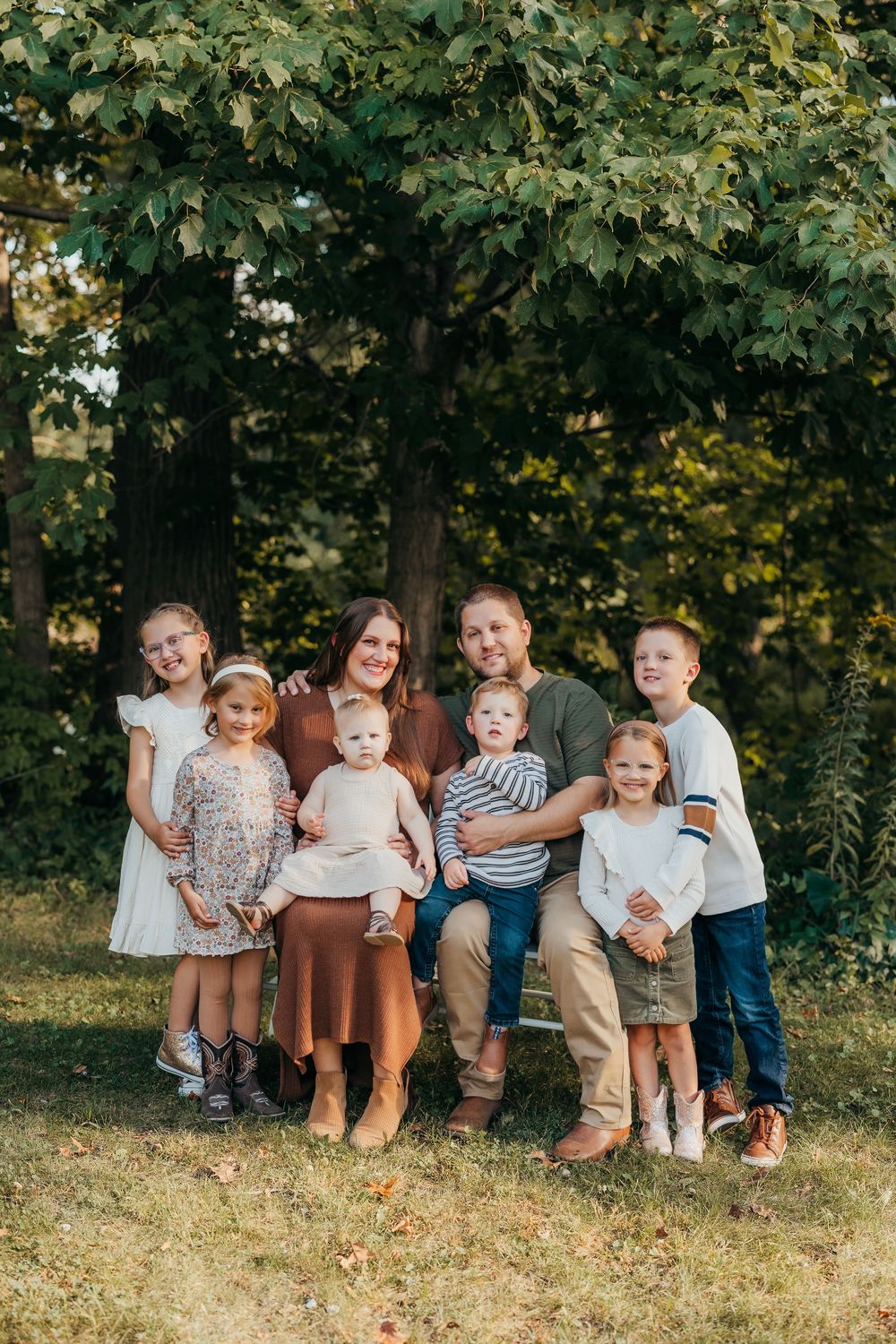 Family group sitting together on grassy hill during autumn photoshoot in casual coordinated outfits.