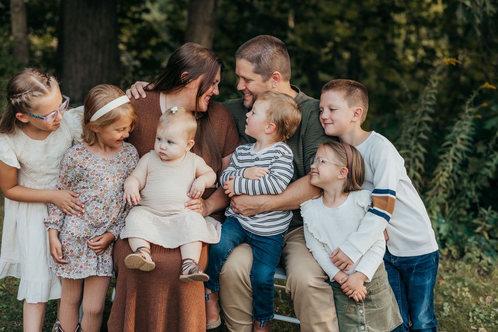 A candid group photo taken outdoors with people interacting and laughing together in a wooded setting.