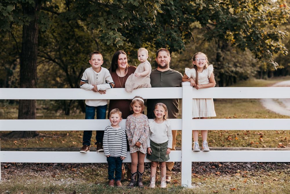 Group portrait by white fence in outdoor park setting during fall season.