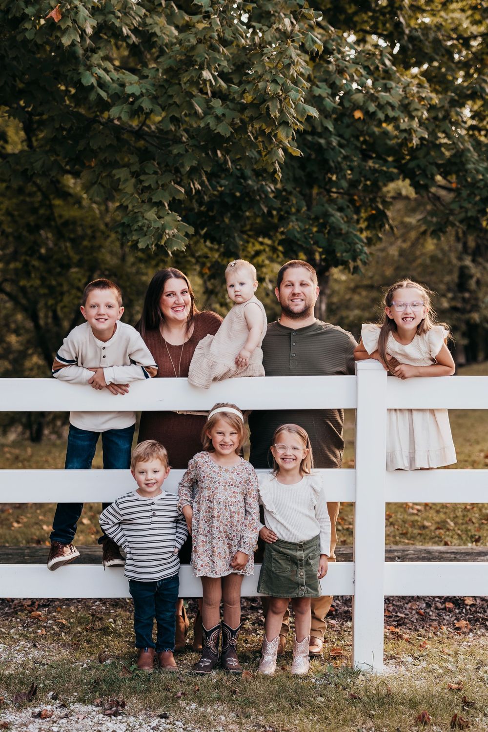 Children and adults gather along a white fence in a fall outdoor setting during a family photo session.