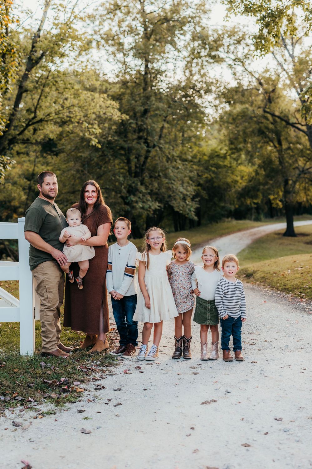 Family group poses together on a winding gravel path surrounded by autumn trees.