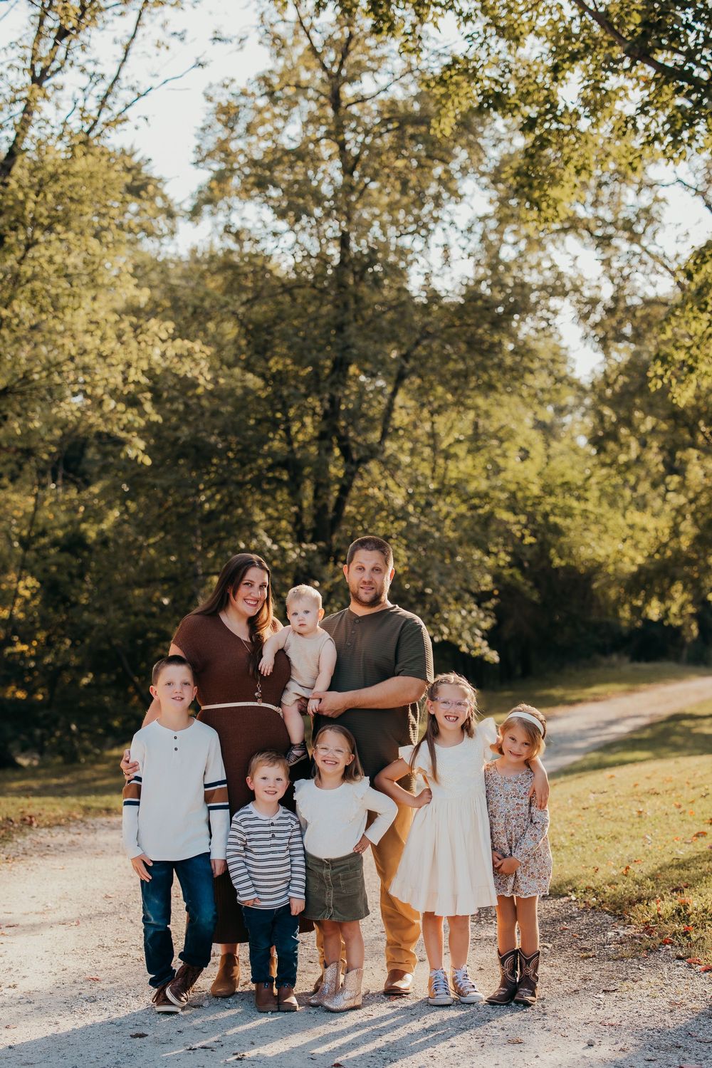 A joyful outdoor family photo session on a dirt path surrounded by trees in warm golden sunlight.