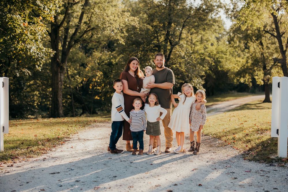Family members stand together on a gravel path with trees in golden afternoon light.