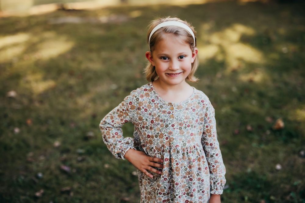 Child wearing floral dress poses outdoors in natural lighting.