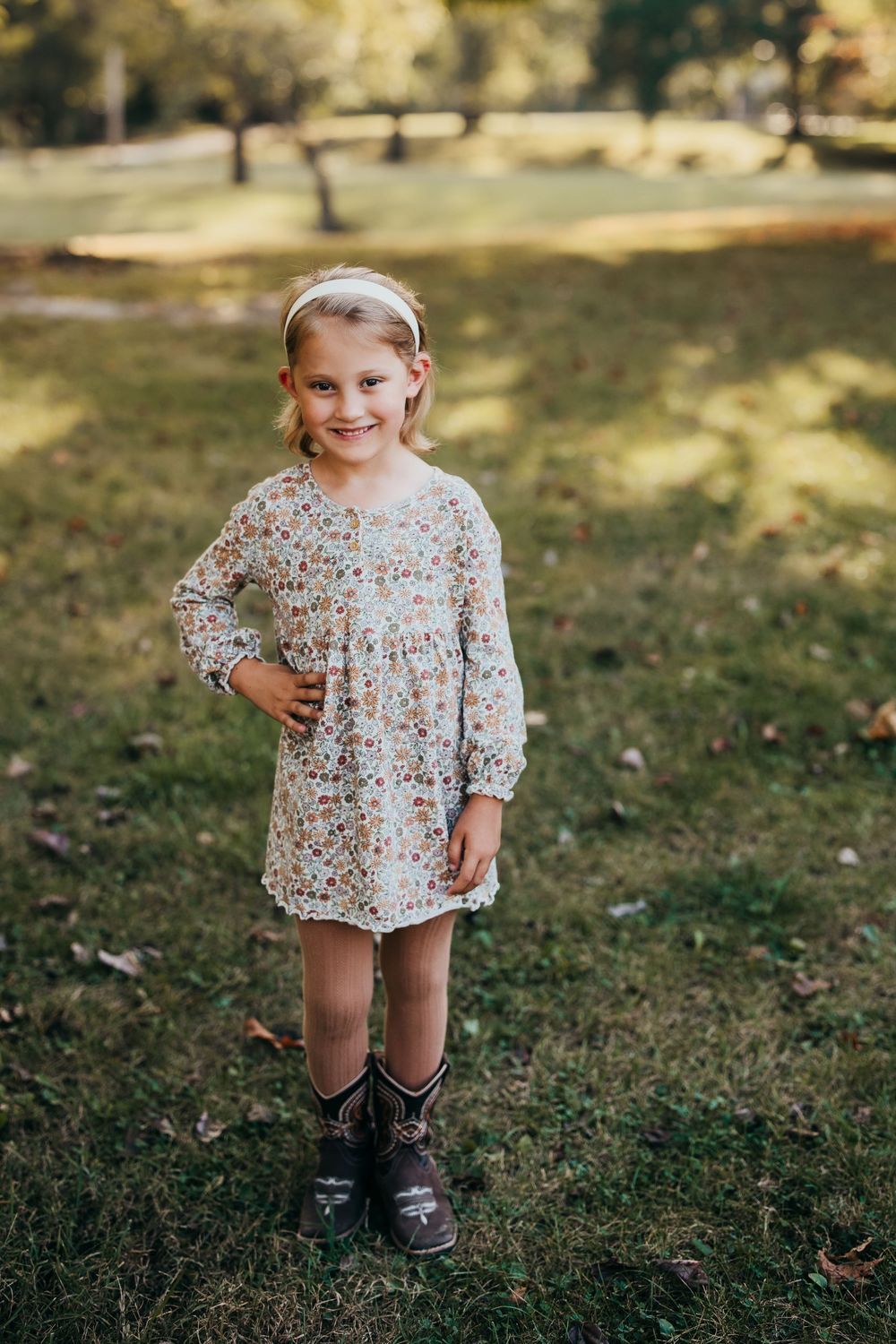 A child in a floral print top and black boots plays outdoors on a sunny autumn day.