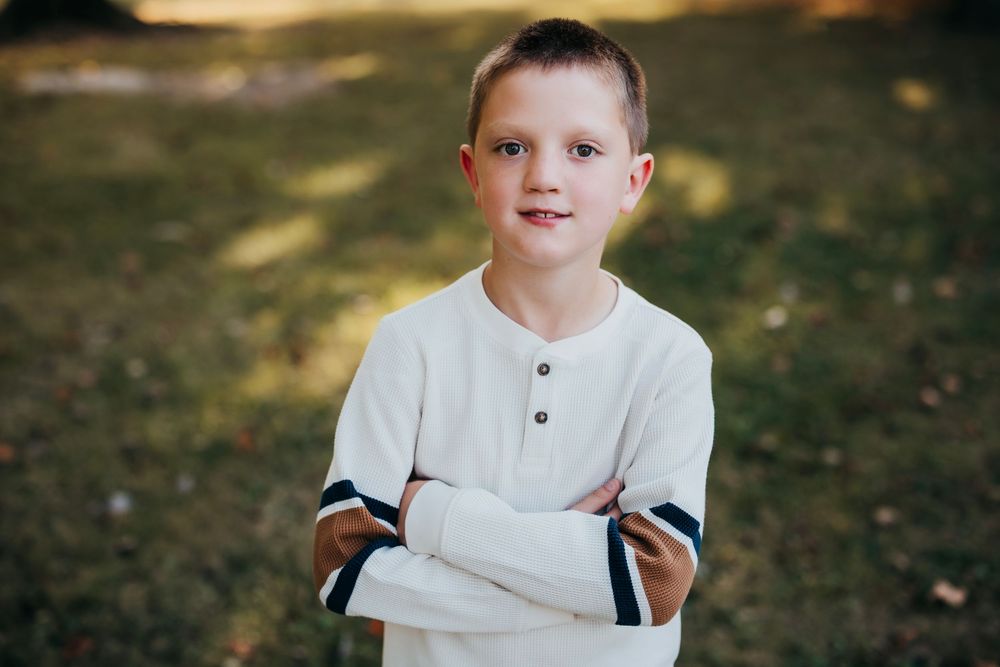 Portrait of a young boy in a white henley shirt against a natural outdoor background.