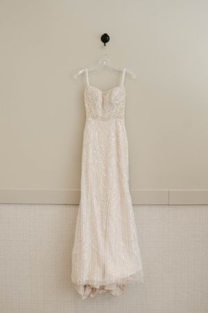 Elegant white lace wedding dress hanging on display against a neutral wall.