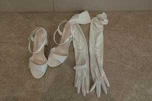 White wedding accessories including long gloves and heeled sandals on beige floor.