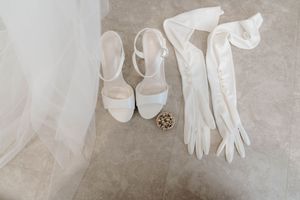 White bridal accessories including gloves and shoes arranged on a beige floor.