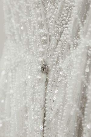 Close-up detail of delicate beading and pearls on white wedding dress fabric.