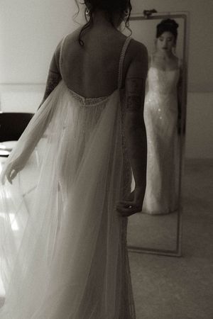 Artistic black and white shot of a bride's back in a flowing wedding dress with mirror reflection.