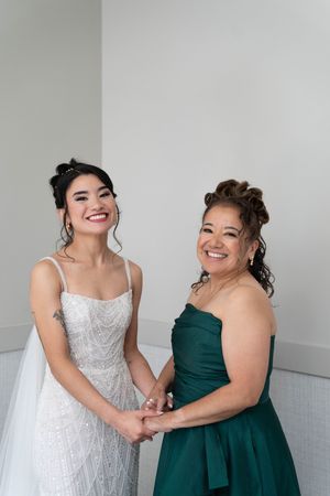 Two women sharing a joyful moment, one in a white gown and another in emerald green.