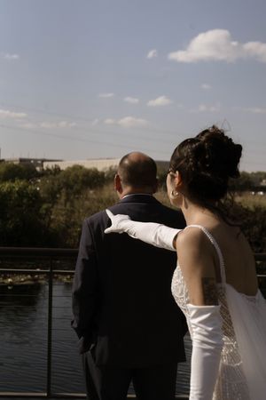 A couple in wedding attire stands together on a deck overlooking a waterfront.