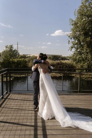 Wedding couple stands together on a wooden boardwalk overlooking a peaceful lake.