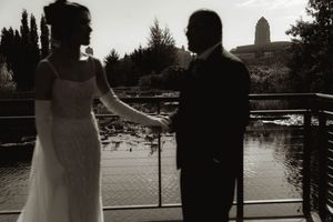 A romantic wedding couple silhouetted against a lake with cypress trees and a tower in the distance.