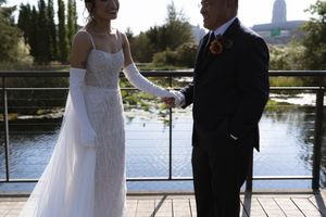 A wedding couple sharing an intimate moment on a deck overlooking a scenic lake and city skyline.