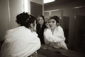 A couple getting ready in a brightly lit room with white decor and mirrors.