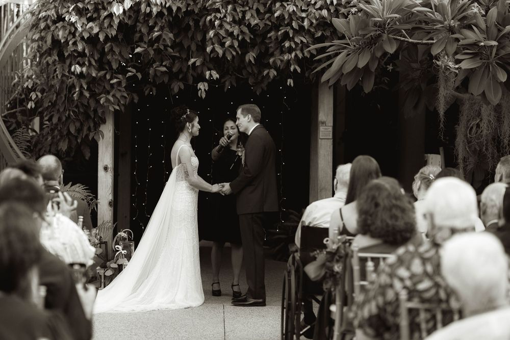 Wedding ceremony taking place in a lush garden setting with white chairs and guests.