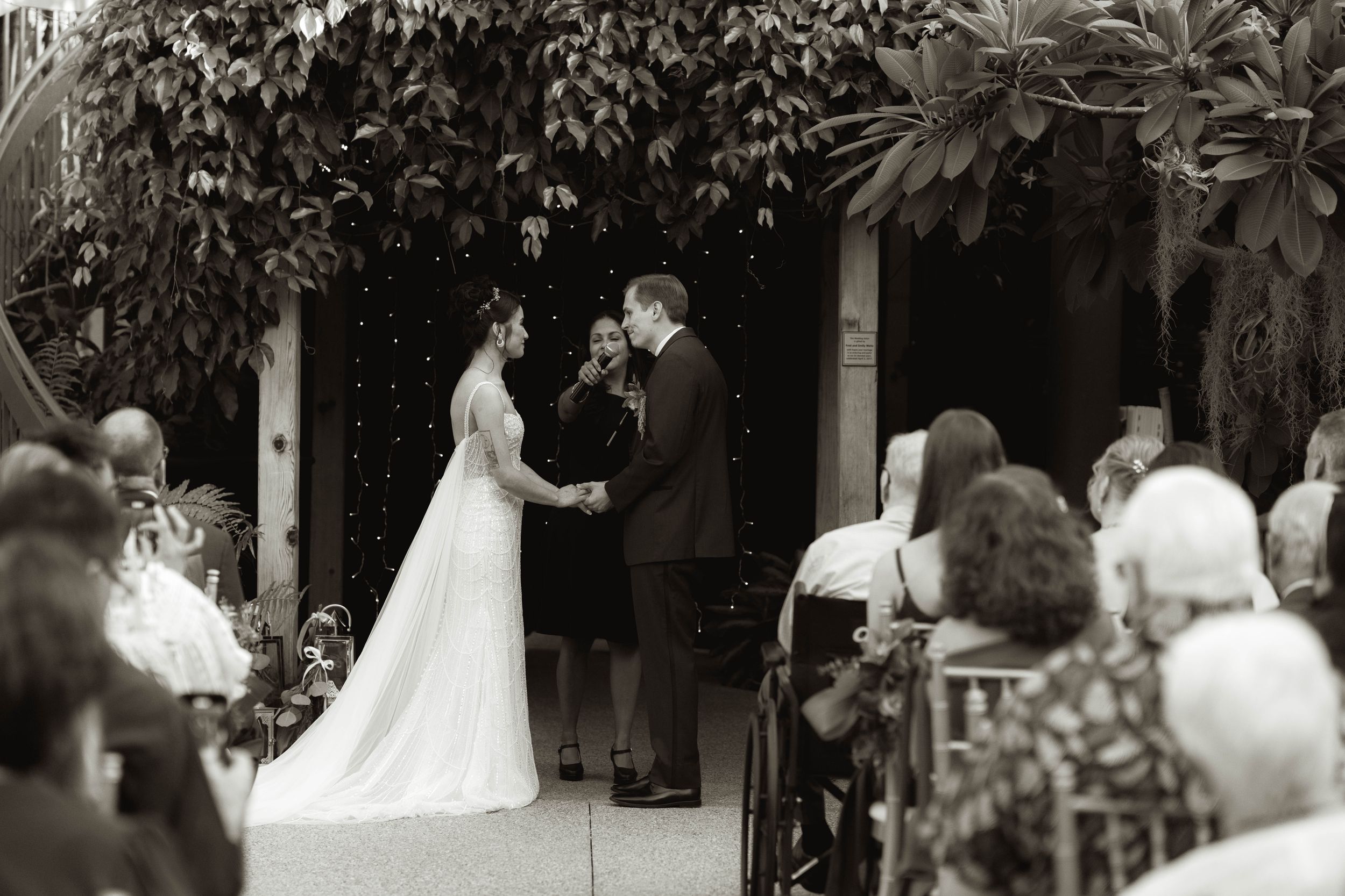 Wedding ceremony taking place in a lush garden setting with white chairs and guests.