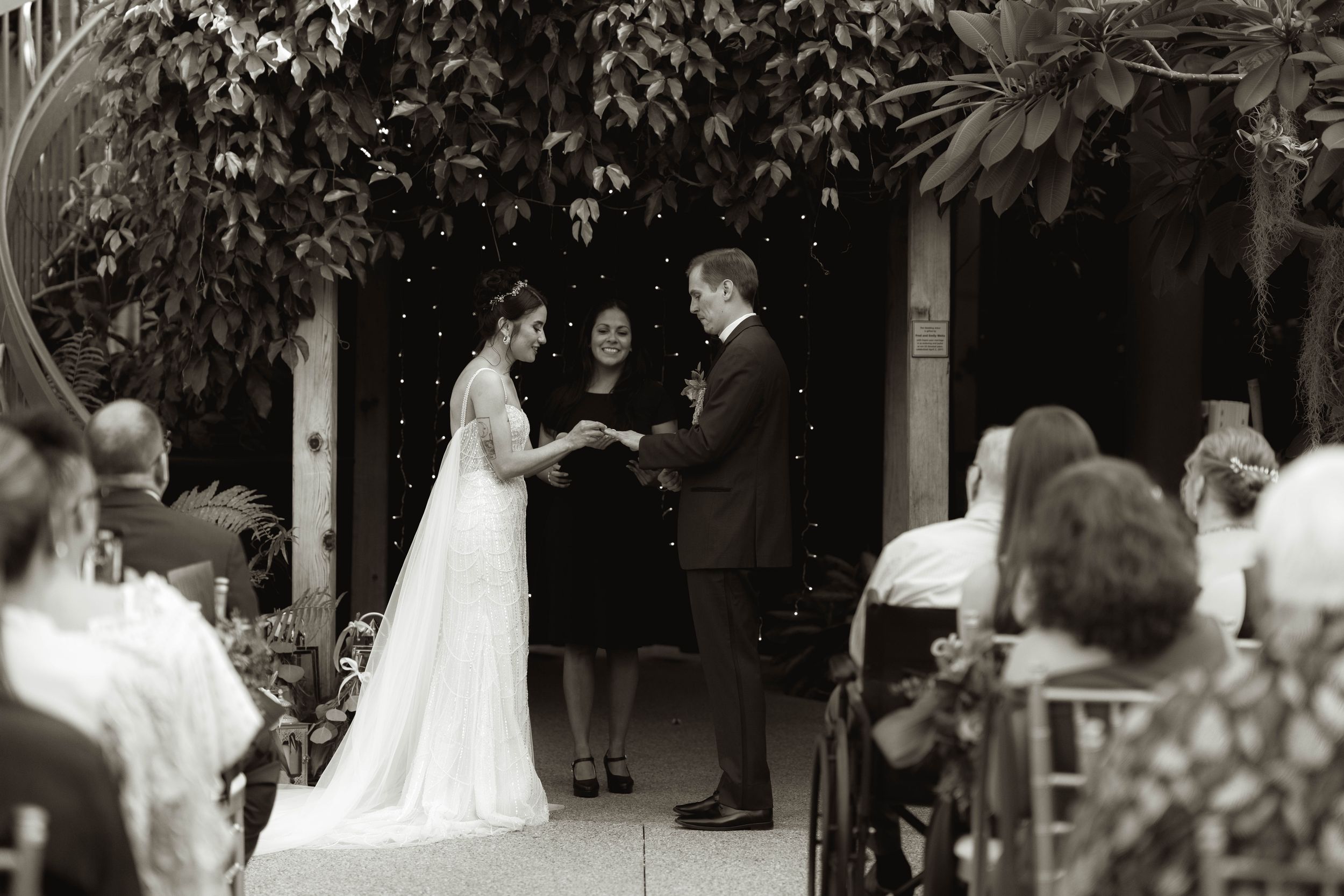 Garden wedding ceremony with natural foliage canopy and white chairs for guests.