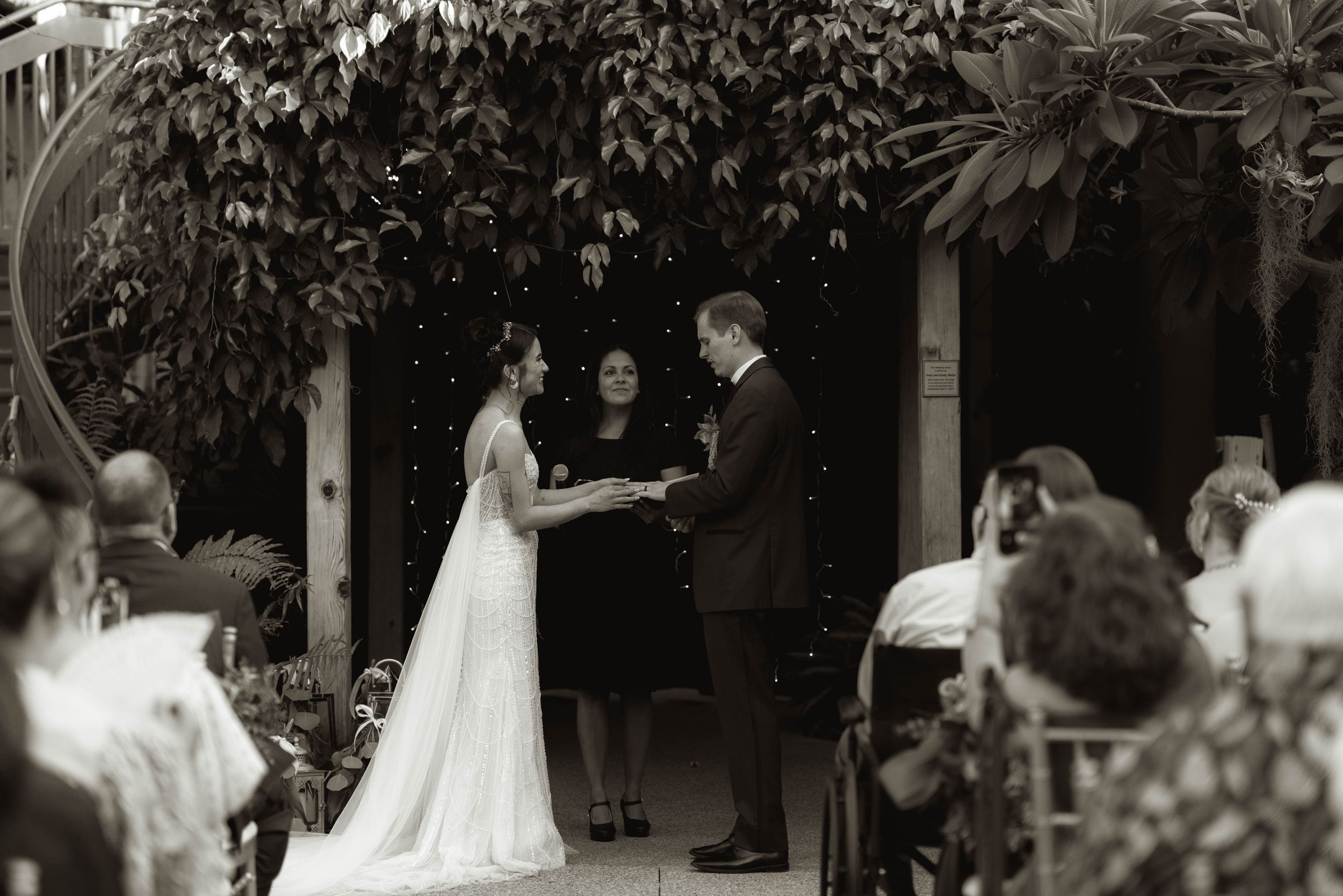 Wedding ceremony moments captured in a garden setting with natural greenery overhead.