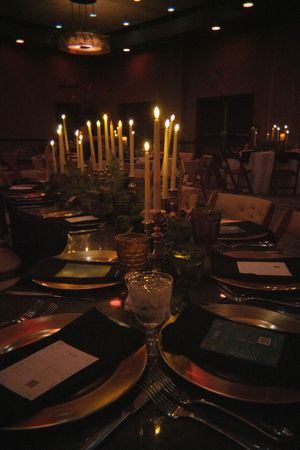 Elegant candlelit reception table settings with golden tapered candles and formal place settings.