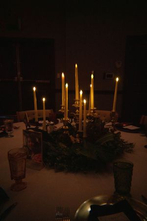 Elegant holiday table setting with lit taper candles and greenery centerpiece in dark moody lighting.
