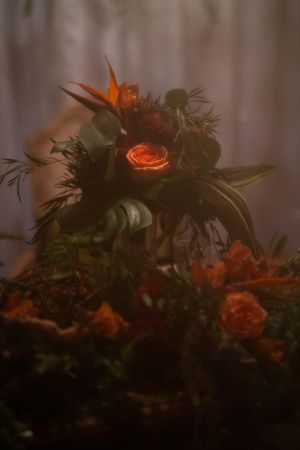 Moody floral arrangement with orange roses and birds of paradise in dark lighting.