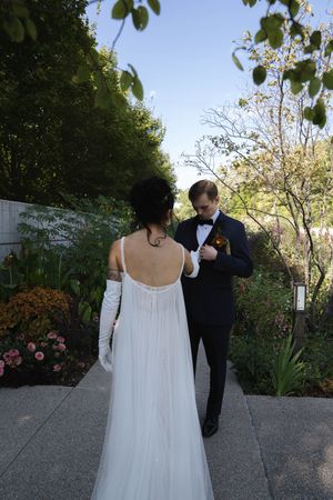 Couple in wedding attire walking through a lush garden path.