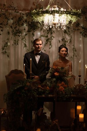 Elegant wedding table setting beneath crystal chandelier with cascading greenery and candlelight.