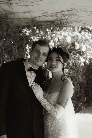 Intimate wedding portrait under a vine-covered pergola in natural light.