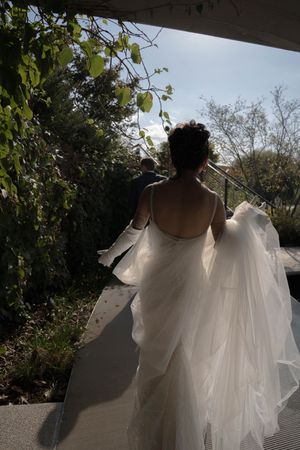 A flowing white wedding dress catches sunlight as it moves through a garden path.