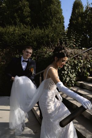 A couple in wedding attire shares a playful moment along a garden railing.