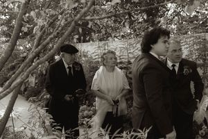 Wedding guests gather under trees during an outdoor garden ceremony.