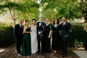 Wedding party gathered outdoors under green trees on a sunny day.