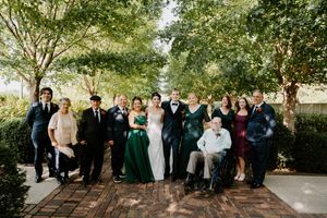 Large wedding party portrait outdoors with trees and brick pathway in background.