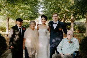 Wedding celebration group photo with formal attire in an outdoor garden setting.