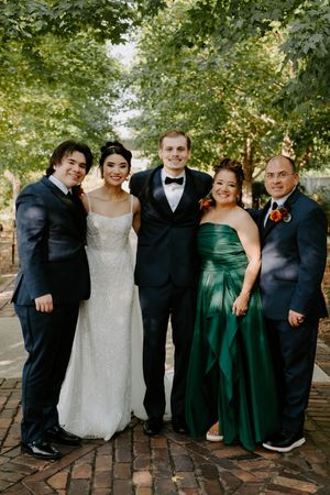 Wedding group portrait featuring emerald green dresses and black suits on brick pathway.