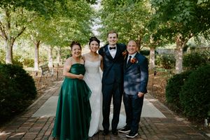 Formal wedding party photo with emerald and black attire under tree canopy.