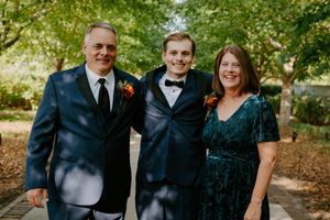 Wedding party members in navy suits and dark dresses gather for formal photos.