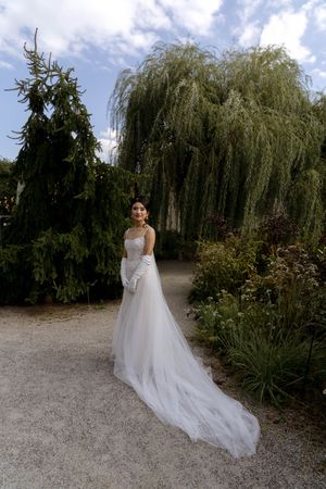 Ethereal bridal portrait with flowing dress against backdrop of weeping willow trees.