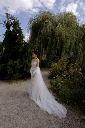 A wedding dress with flowing tulle skirt photographed in a garden setting with weeping willow trees.