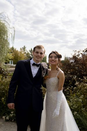 A wedding couple poses together outdoors under cloudy skies.