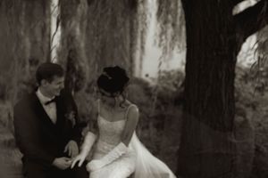 Black and white wedding photo captures intimate moment between couple under willow trees.