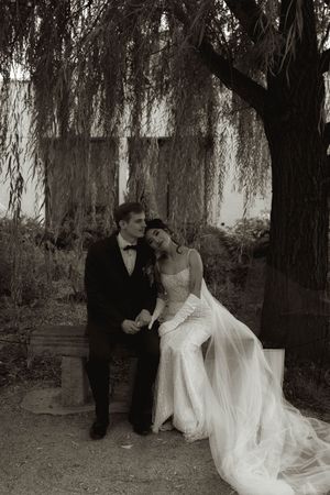 Artistic black and white wedding portrait shows couple's intimate moment under willow branches.