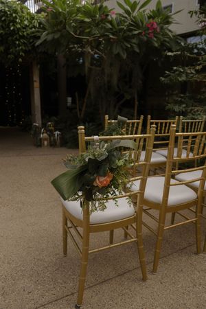 Gold chiavari chairs with white cushions set up for wedding ceremony with floral decorations.