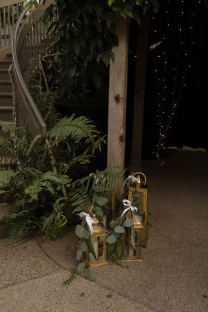 Rustic wedding decor features lanterns and greenery arrangements along garden pathway.