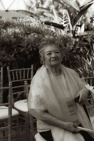 An elderly guest in a light-colored outfit sits in a garden setting with bamboo chairs.