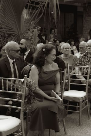 Wedding guests seated in formal attire at an outdoor reception with bamboo chairs.