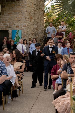 Wedding ceremony guests seated in rows of bamboo chairs at an outdoor venue with stone walls.